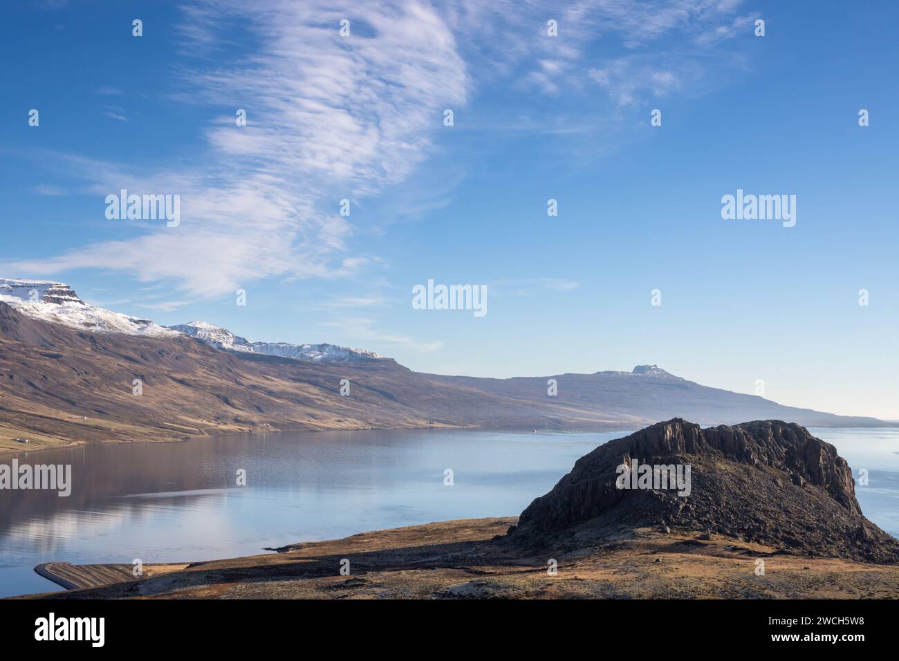 Giornata di sole con cielo blu e nuvole di luce. Fiordo circondato da prati e montagne con un colore autunnale della vegetazione. Eskifjordur, Icelan orientale Foto Stock