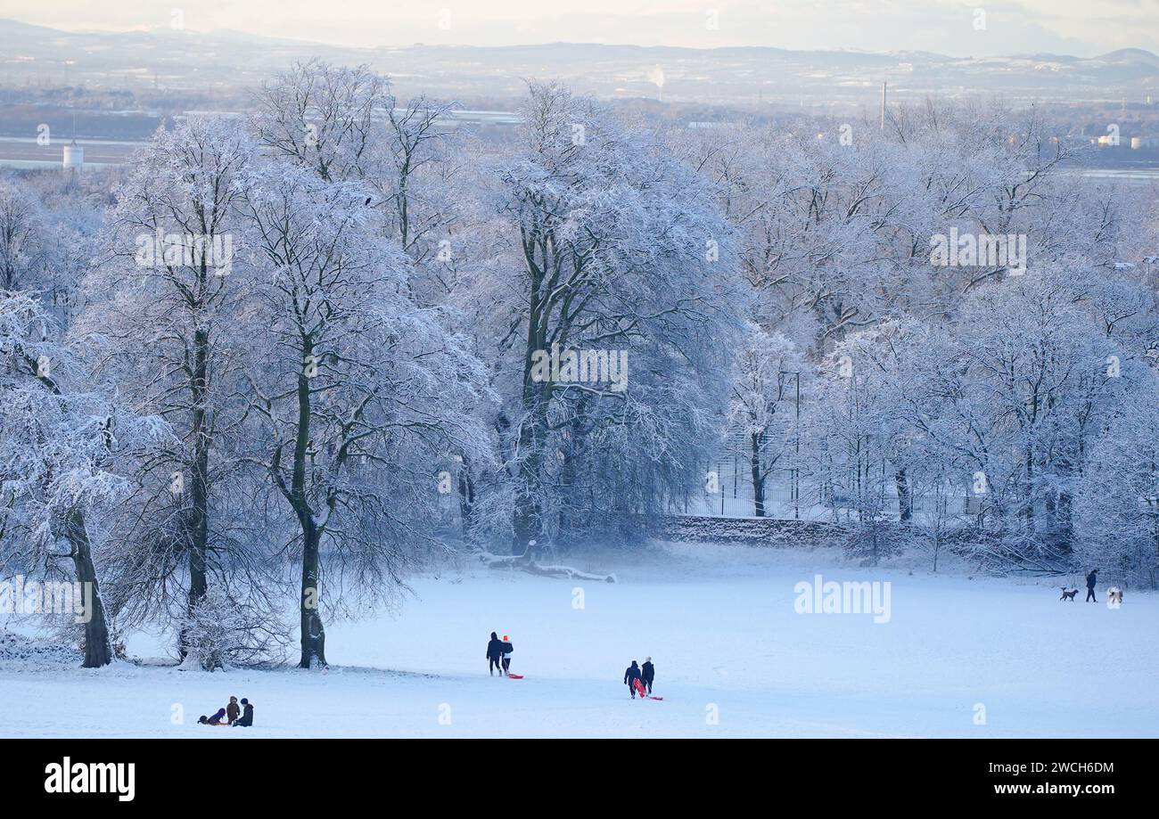 Le persone approfittano del tempo innevato con le slitte a Camp Hill a Woolton, Liverpool. Gran parte della Gran Bretagna sta affrontando un'altra giornata di basse temperature e di interruzioni dei viaggi dopo che i bassi della notte sono scesi sotto il congelamento per la maggior parte del paese. Un "tuffo freddo dell'aria artica” si è spostato a sud in tutto il paese negli ultimi giorni, rendendolo 5C-6C più basso del solito per questo periodo dell'anno, ha detto l'Ufficio MET. Data immagine: Martedì 16 gennaio 2024. Foto Stock