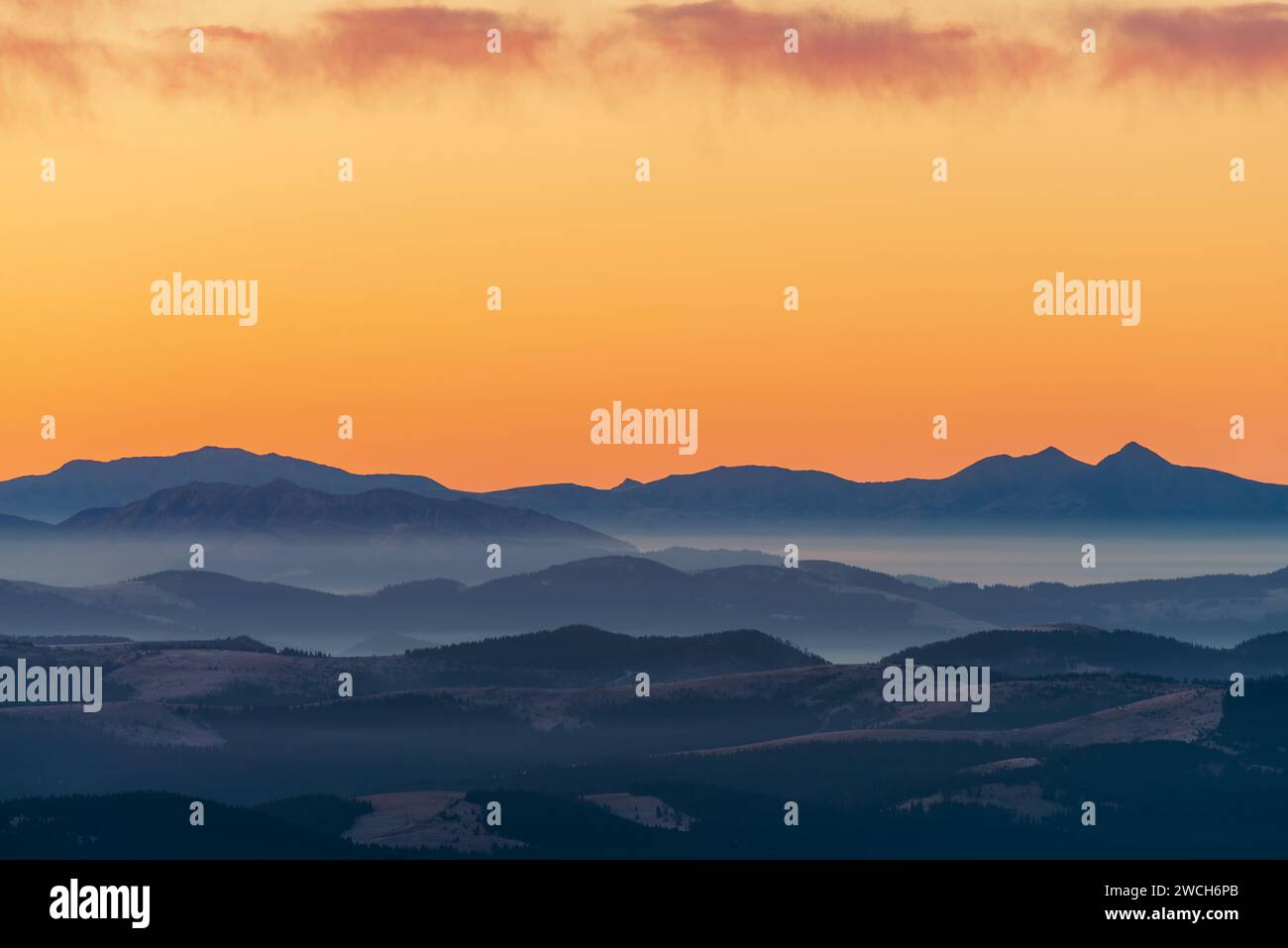 Una vista straordinaria delle montagne coperte di neve e nebbia contro il cielo arancione. Un concerto di libertà e bellezza della natura. Foto Stock