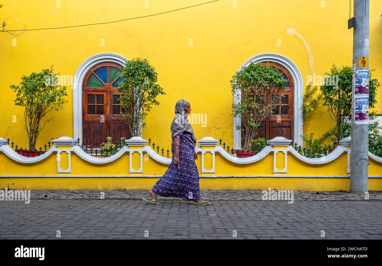 Scena di strada con una donna indiana di fronte alla casa gialla, Fort Kochi, Cochin, Kerala, India Foto Stock