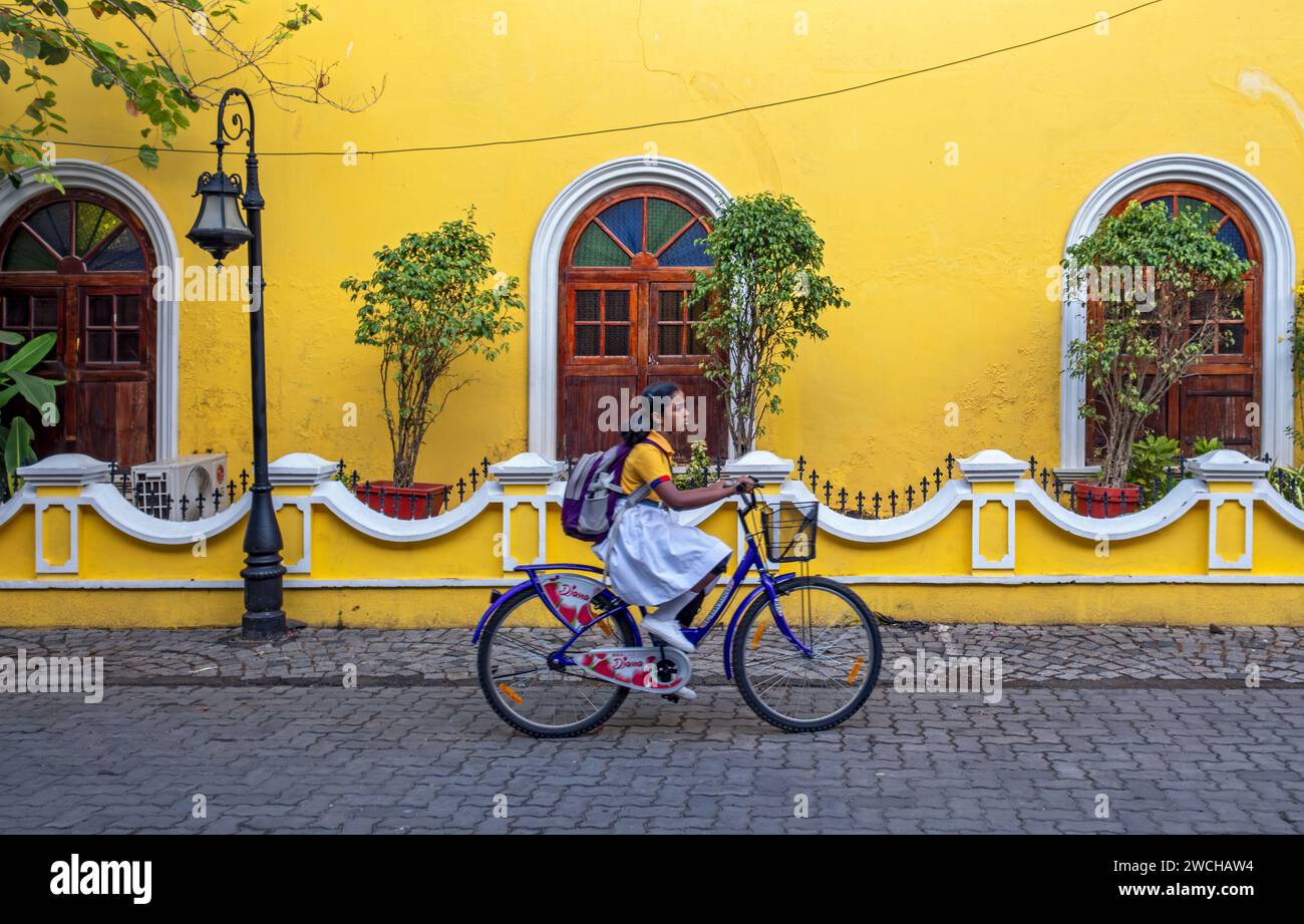 Scena di strada con ragazza in bicicletta di fronte alla casa gialla, Fort Kochi, Cochin, Kerala, India Foto Stock