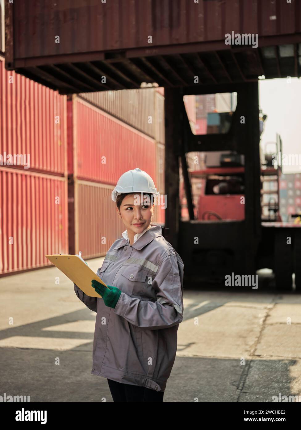 giovane lavoratrice asiatica che indossa un casco di sicurezza e lavora con la scatola del contenitore presso il cantiere di spedizione Foto Stock