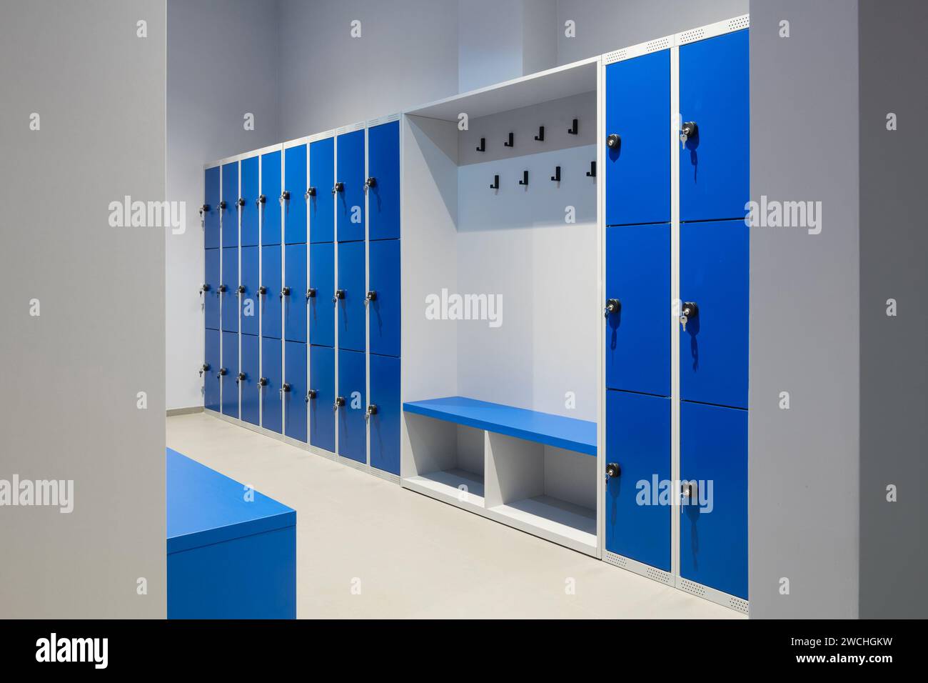 Una fila di armadietti blu su una parete con chiave in una serratura e un banco Foto Stock