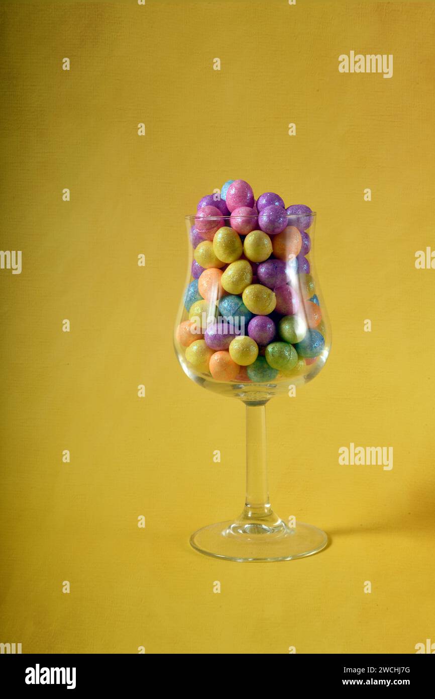 Foto verticale di piccole uova di Pasqua colorate in un bicchiere di vino. Copia spazio a sinistra. Livello texture digitale aggiunto alla foto. Foto Stock