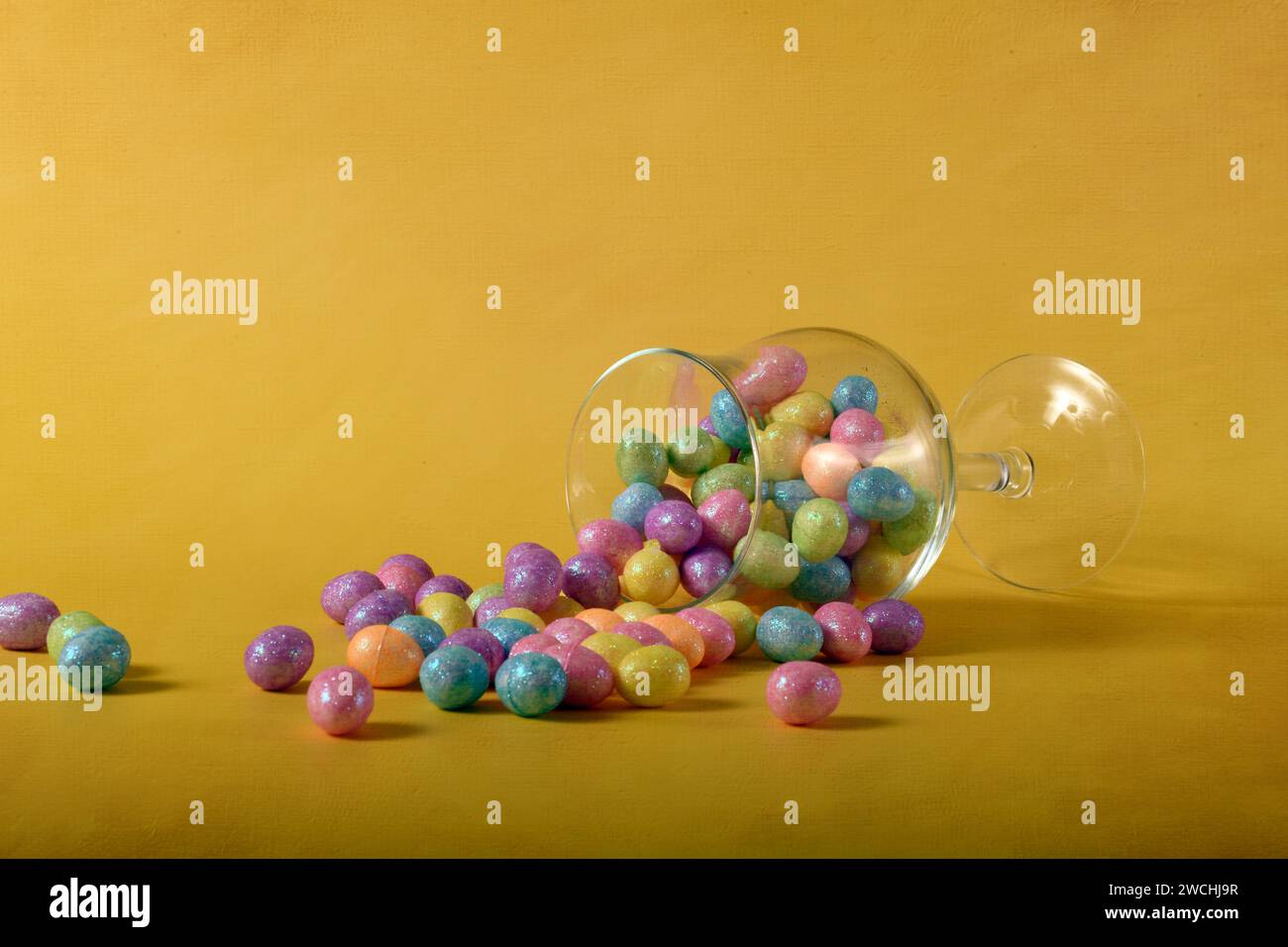 Uova di Pasqua dai colori pastello e glitter che fuoriescono da un bicchiere. Spazio di copia nella parte superiore della foto. Foto Stock
