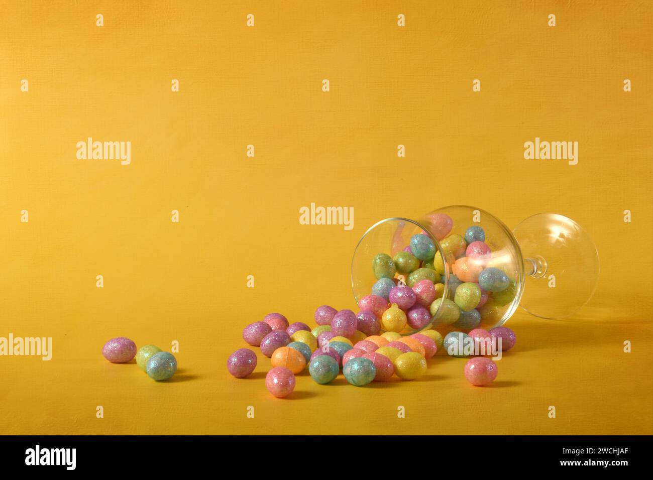 Uova di Pasqua da un bicchiere su sfondo giallo. Foto orizzontale con livello texture digitale e spazio di copia. Foto Stock