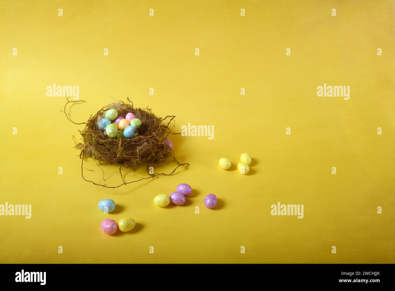 Nido di uccello Tny con piccole uova di Pasqua color pastello. Foto orizzontale su sfondo giallo. Copia spazio a destra. Foto Stock