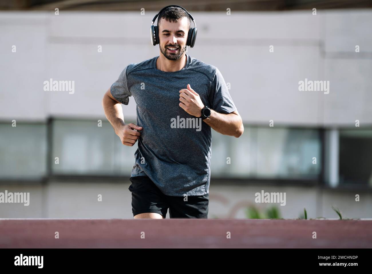 Uomo sportivo che corre indossando cuffie all'aperto. Giovane atleta maschile che ascolta musica durante l'allenamento di fitness. Foto Stock
