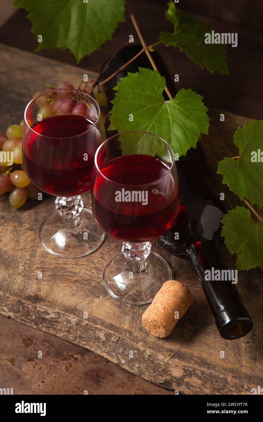 Il concetto di una deliziosa bevanda alcolica, vino e uva. Bottiglia di vino, bicchieri di vino rosso e mazzo d'uva su fondo rustico scuro di legno Foto Stock