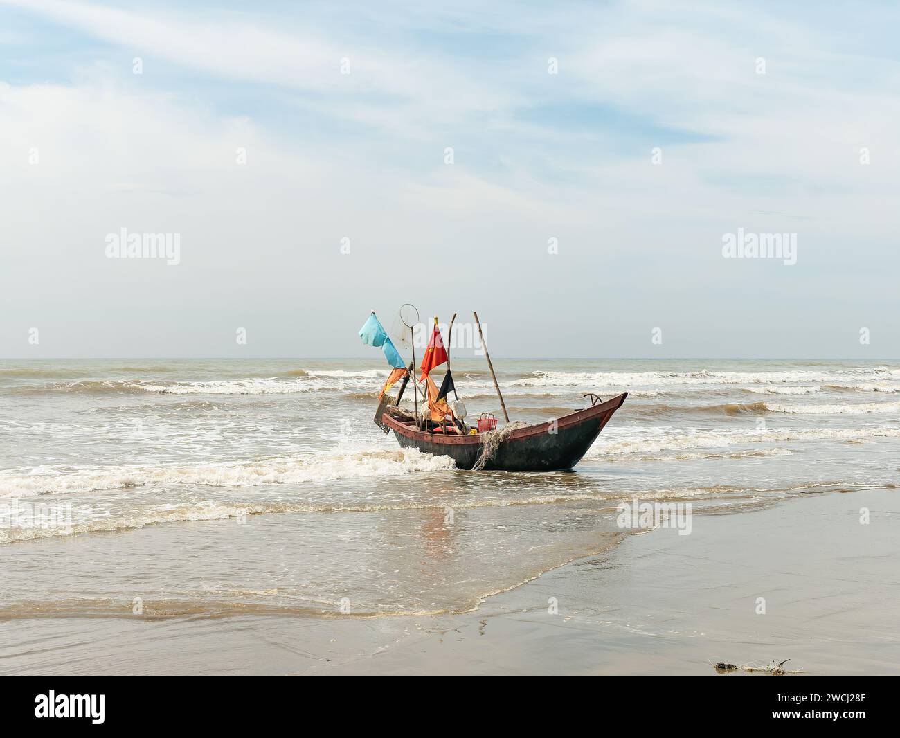 Barca da pesca a Sam Son Beach, Thanh Hoa, Vietnam sulla spiaggia alla fine della giornata di lavoro, pronta per essere trasportata più in alto sulla spiaggia. La barca è costruita Foto Stock