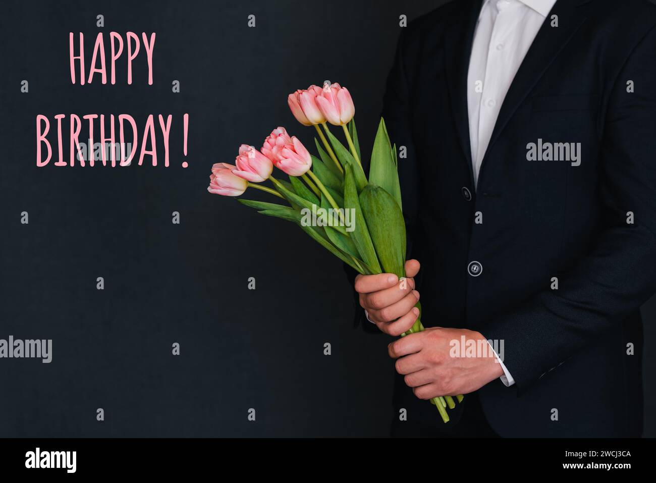 Bouquet di fiori rosa di tulipani nelle mani degli uomini in un completo. Biglietto d'auguri con l'iscrizione buon compleanno Foto Stock