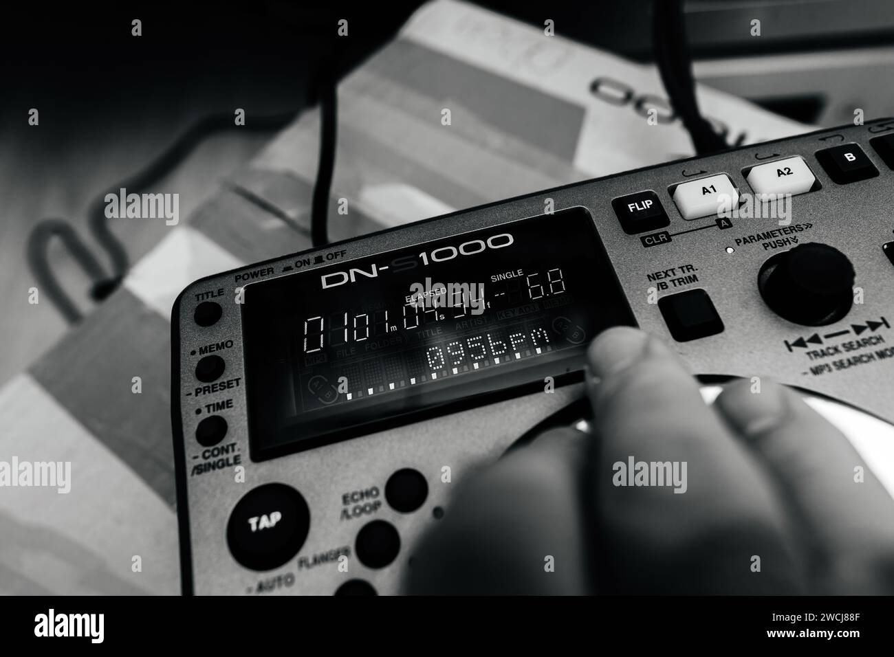 Parigi, Francia - 24 ottobre 2023: Una mano maschile sulla nuova attrezzatura di mixaggio DJ Denon DN-S1000, test a ritmo di 095 BPM dopo l'unboxing, in una scena in bianco e nero Foto Stock