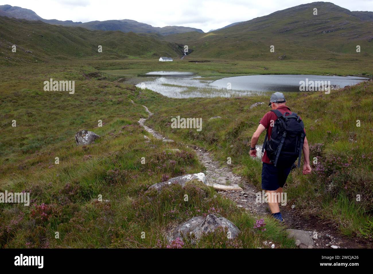 Else Man Walking on Path to 'Lochan An asgair' e The Scottish Mountaineering Club's Ling Hut a Glen Torridon, Scottish Highlands, Scozia, Regno Unito. Foto Stock