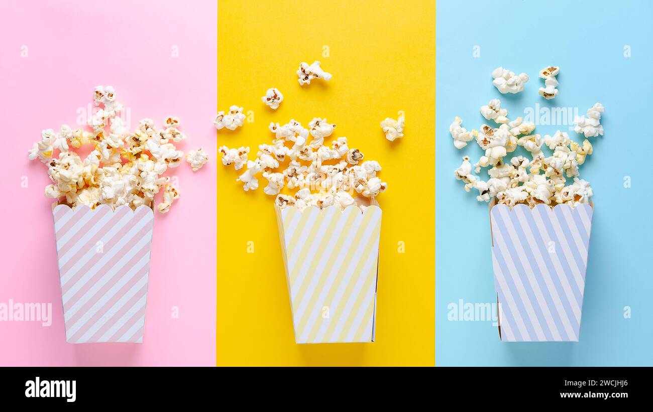 Tre secchi a strisce di popcorn su sfondo rosa, giallo e blu, vista dall'alto e spazio per la copia. Foto Stock