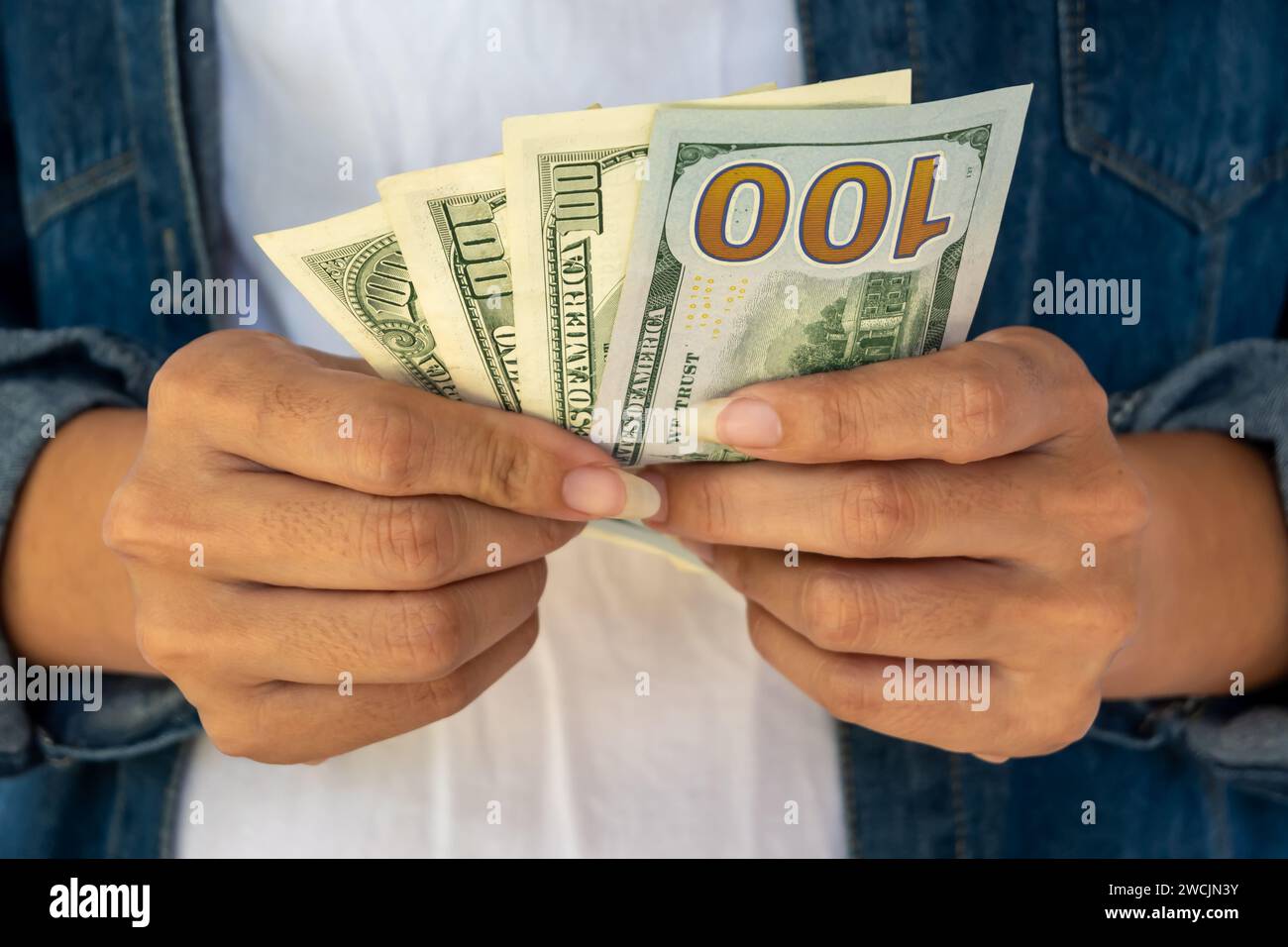Le mani di una donna che regge banconote da 100 dollari, e' di fronte al fronte che tiene con due mani. Foto Stock
