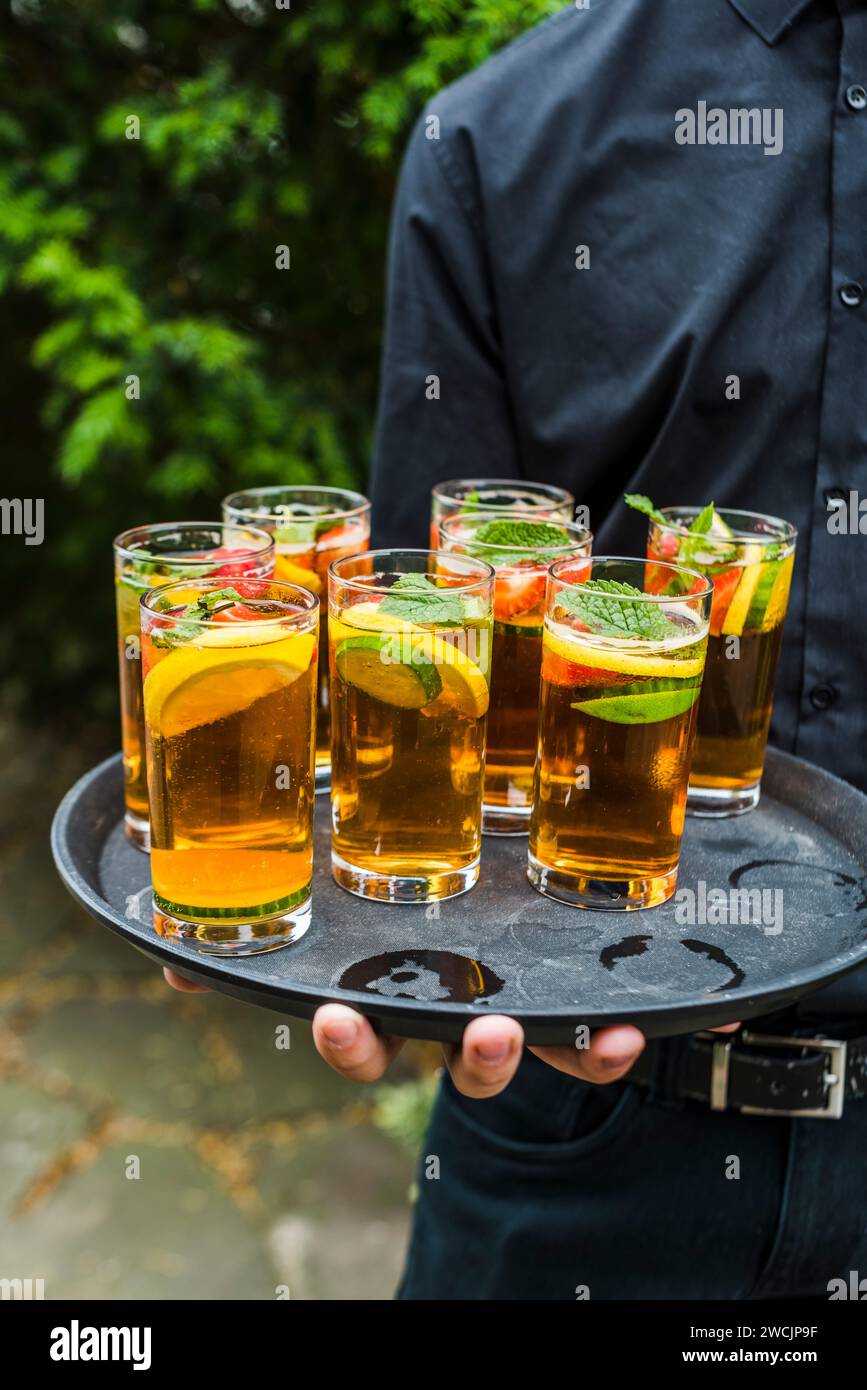 Un server che tiene cocktail Pimm's in occasione di un evento all'aperto. Foto Stock