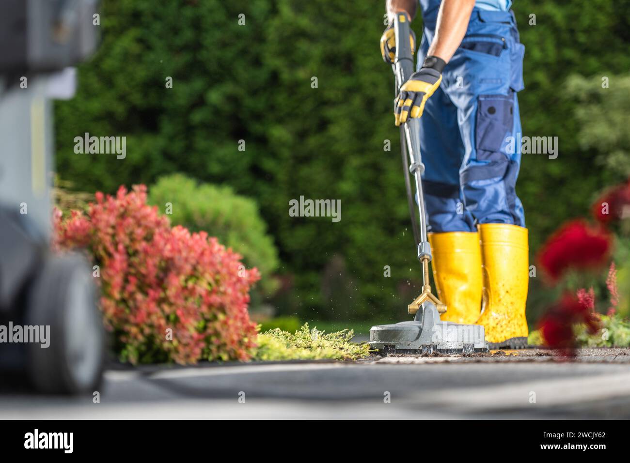 Uomo caucasico che lava il vialetto residenziale utilizzando l'idropulitrice Foto Stock