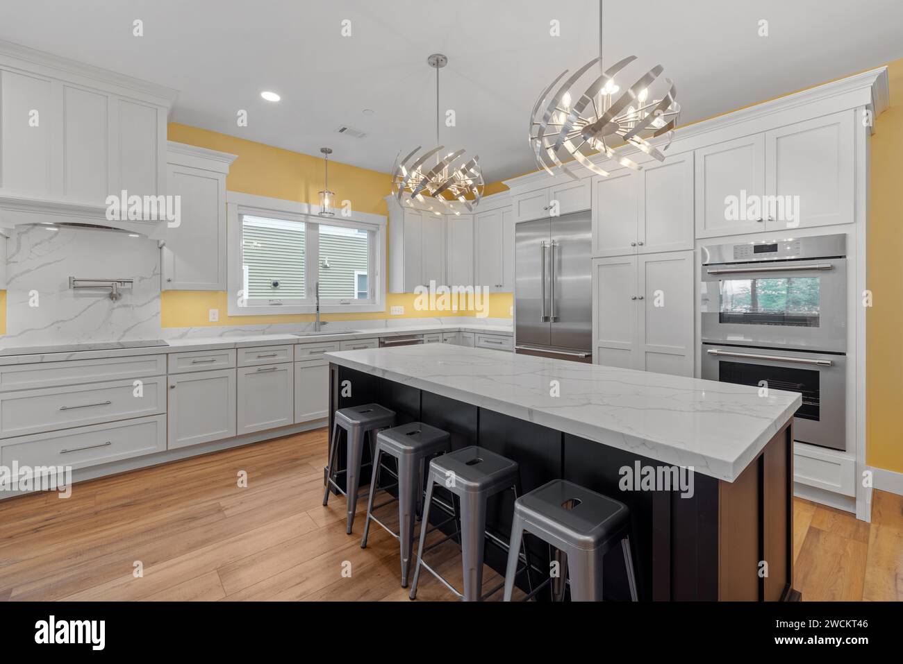 Cucina con isola centrale, pavimenti in legno e armadietti bianchi Foto Stock