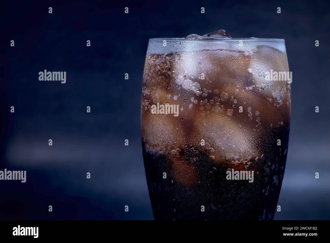 Bicchiere di cola fresca con ghiaccio, bollicine e spumante. Dolce fresco freddo con cubetti di ghiaccio. Bicchiere di cola con rinfresco estivo su nero. Foto Stock