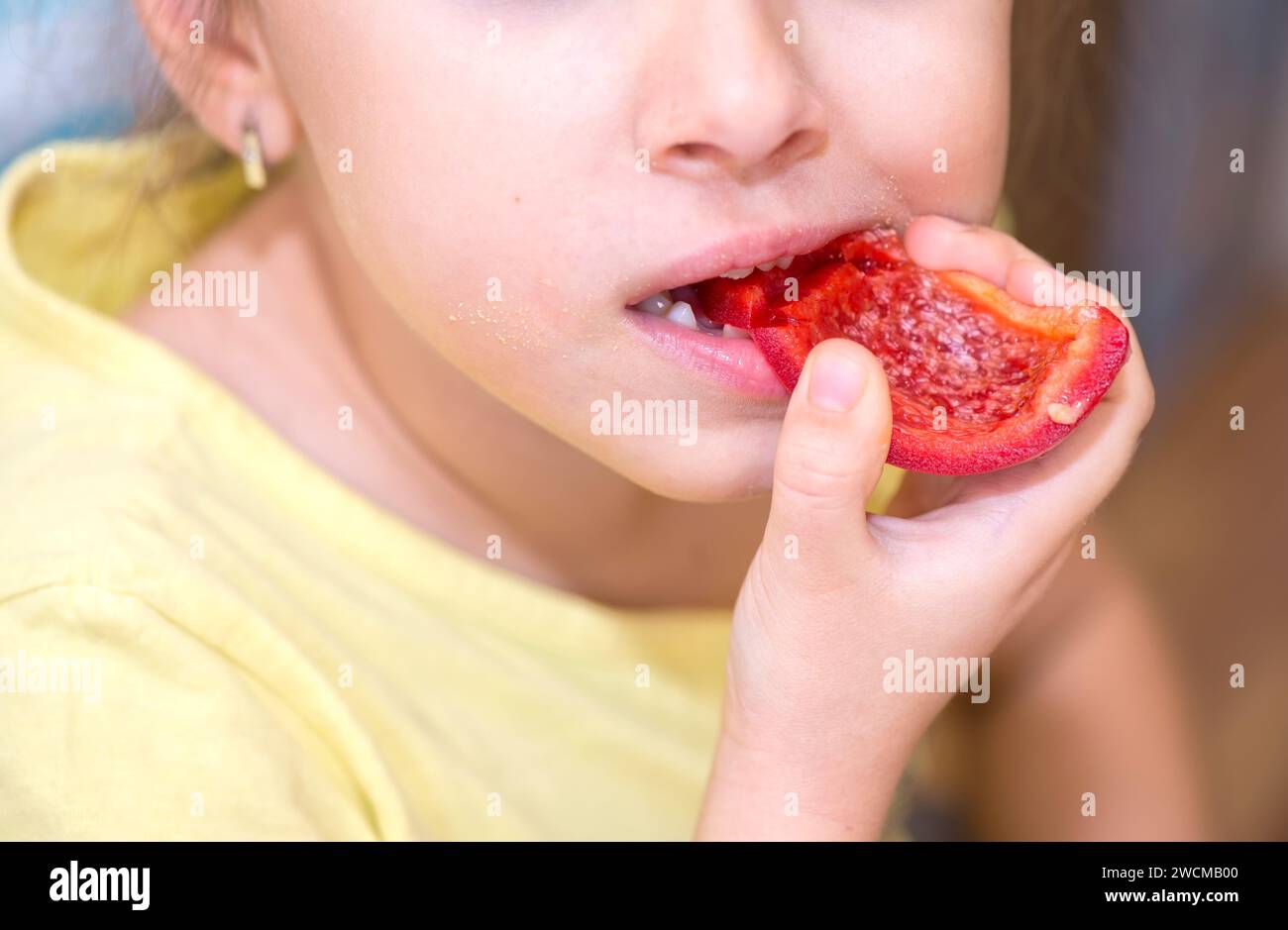 Primo piano di una bocca di una bambina caucasica che mangia pepe rosso Foto Stock