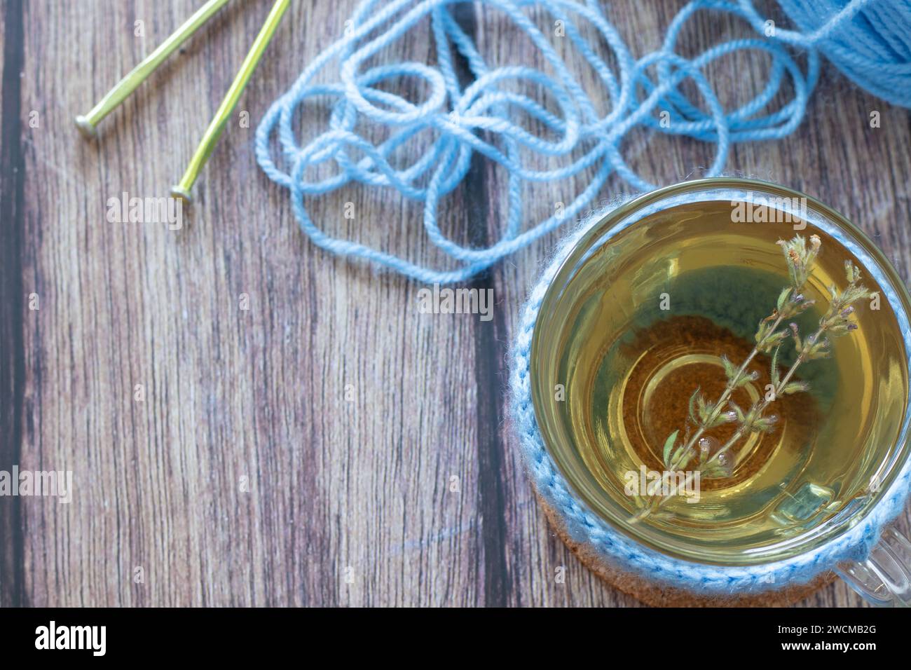 Tazza di tè caldo alle erbe con filo blu e aghi per maglieria su legno. Vista dall'alto. Concetto di hobby creativo. Foto Stock