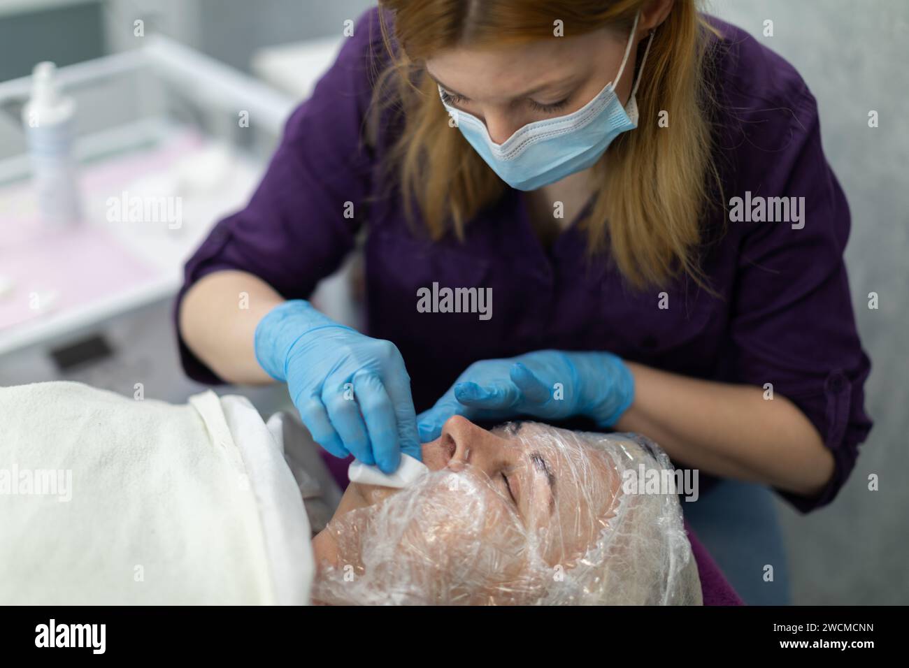 Il cosmetologo lava la pelle del paziente con una garza. Foto Stock