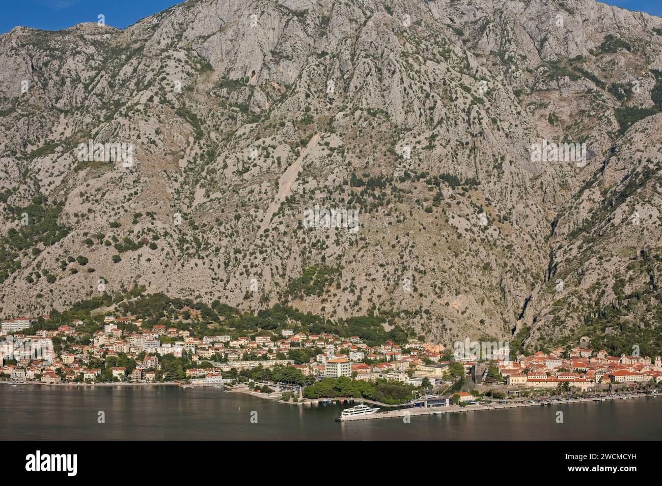Il pittoresco villaggio di Cattaro in Montenegro si annida lungo la tranquilla baia, con le maestose montagne balcaniche che si innalzano sullo sfondo. Foto Stock