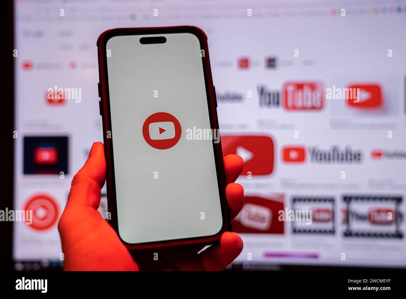 Uomo con smartphone iPhone 14 Pro Max con app YouTube davanti al monitor in ufficio. Vista dall'alto. Spia rossa bassa. Budapest, Ungheria. Novem Foto Stock