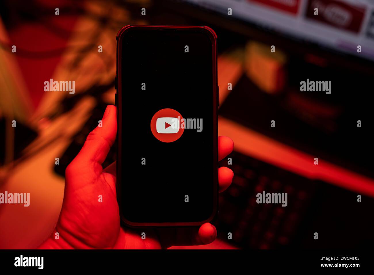 Uomo con smartphone iPhone 14 Pro Max con app YouTube davanti al monitor in ufficio. Vista dall'alto. Spia rossa bassa. Budapest, Ungheria. Novem Foto Stock