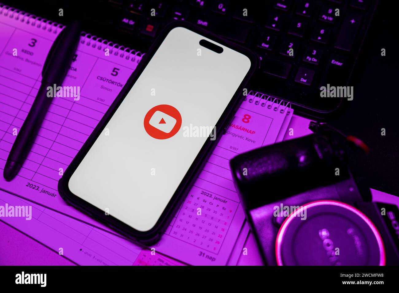 Smartphone Apple iPhone 14 Pro Max con logo YOUTUBE. YouTube è un sito Web per la condivisione di video. Luce soffusa viola, ambiente d'ufficio. Budapest, Hu Foto Stock