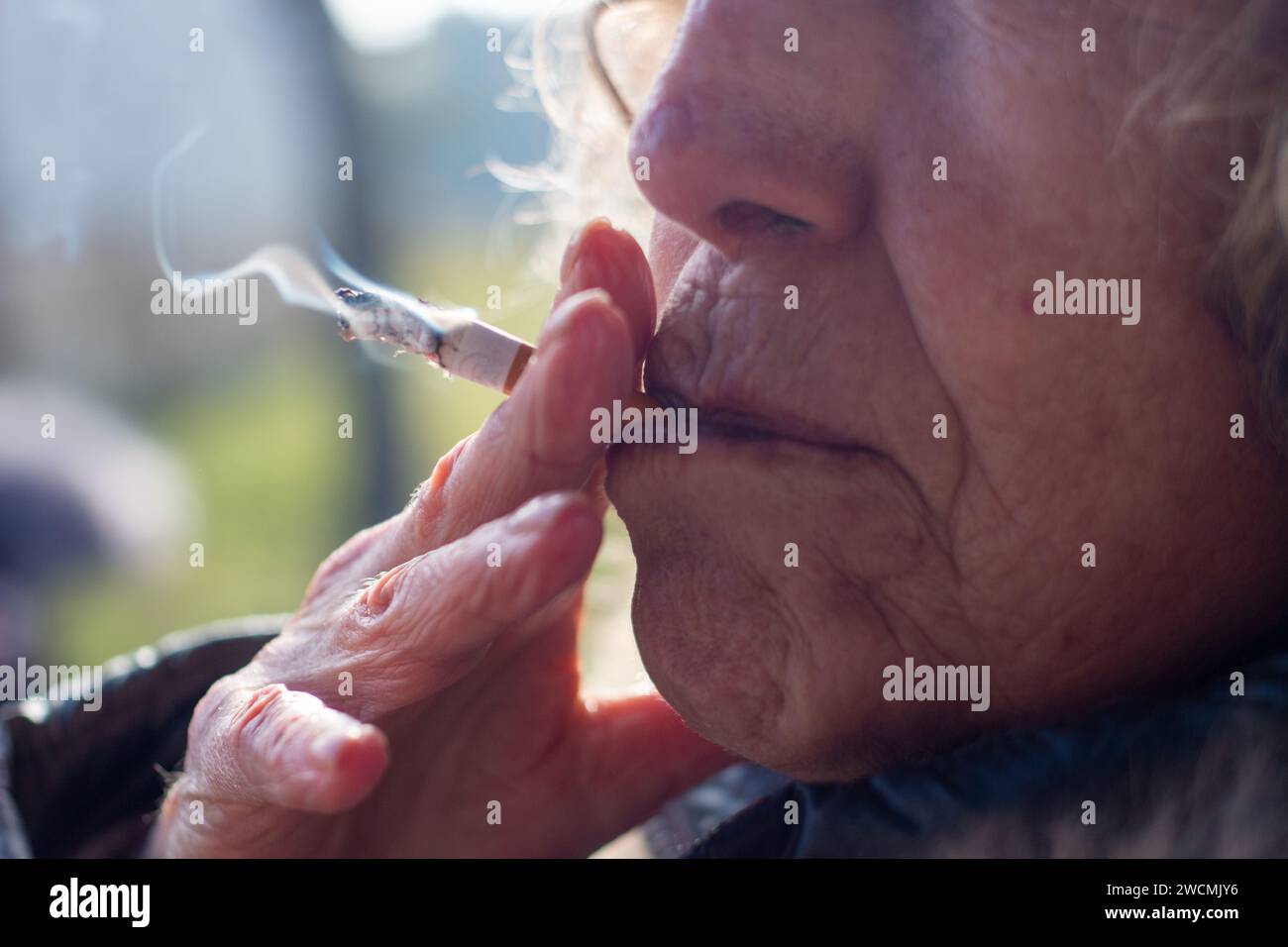 Bocca di una donna anziana anonima che si prende una leggera scossa su una sigaretta che fuma Foto Stock