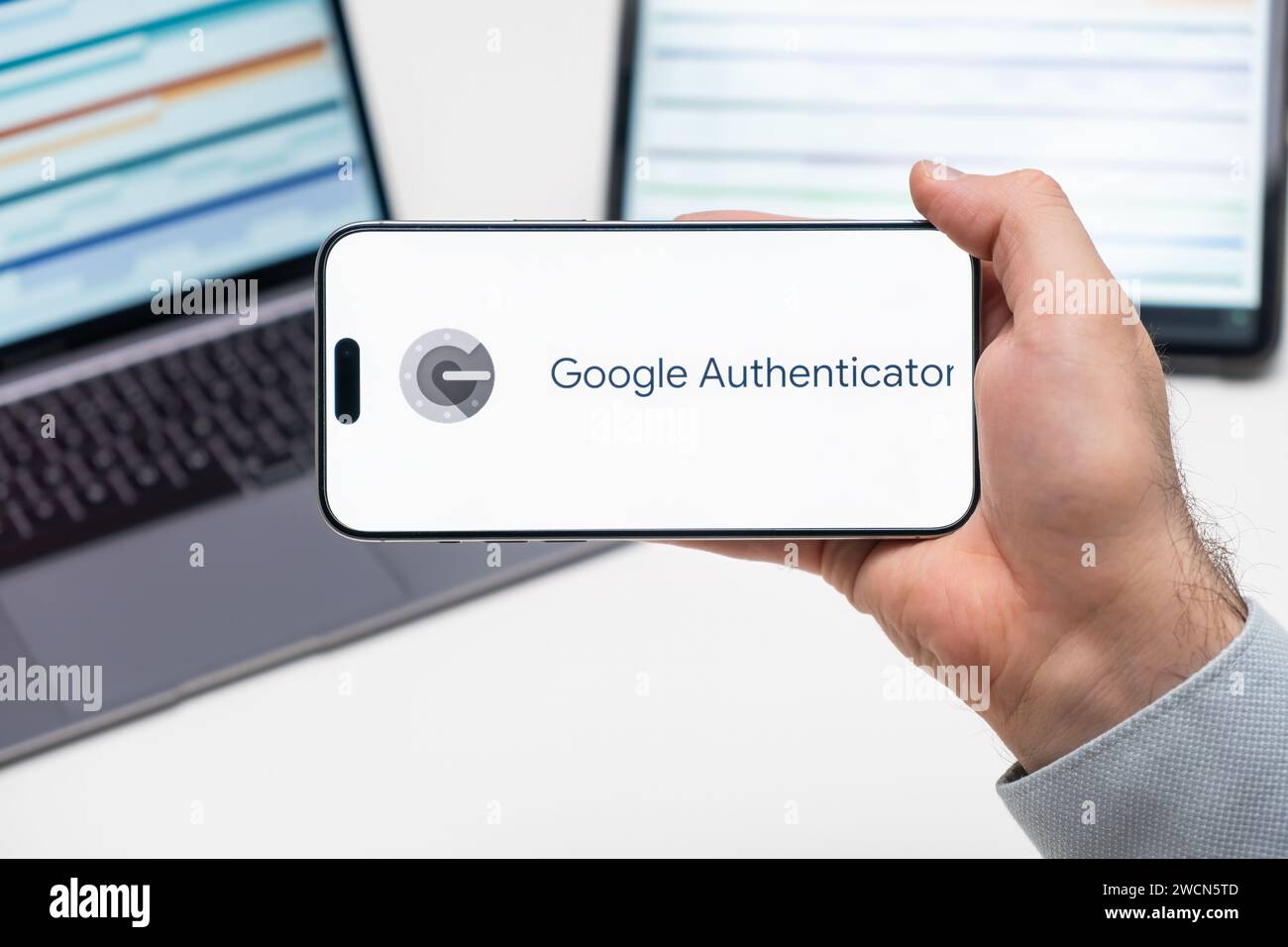 Logo Google Authenticator dell'app sullo schermo del telefono cellulare tenuto dall'uomo davanti al laptop e al tablet, dicembre 2023, Praga, Repubblica Ceca Foto Stock