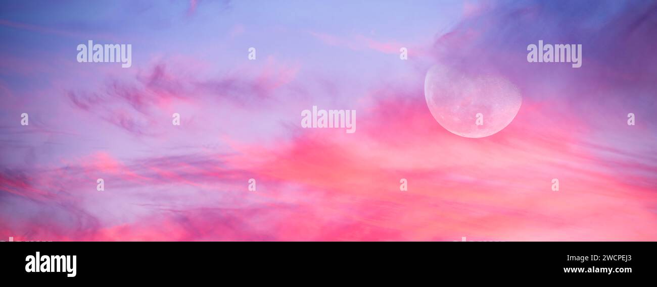 Una luna piena si alza in Una colorata intestazione Twilight Sky al tramonto Foto Stock