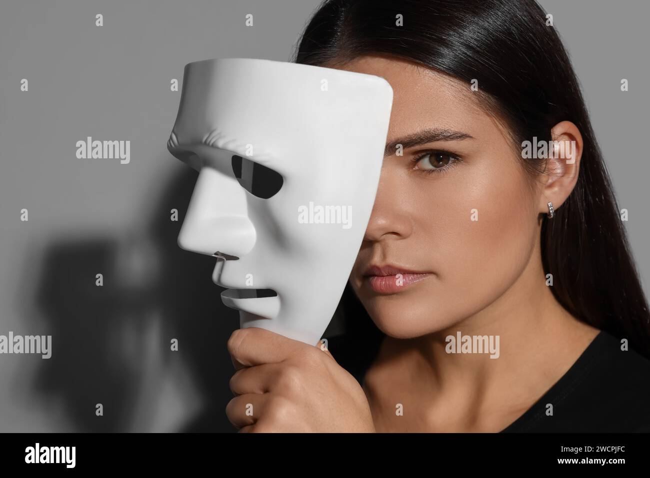 Concetto di personalità multipla. Donna con maschera su sfondo grigio Foto Stock