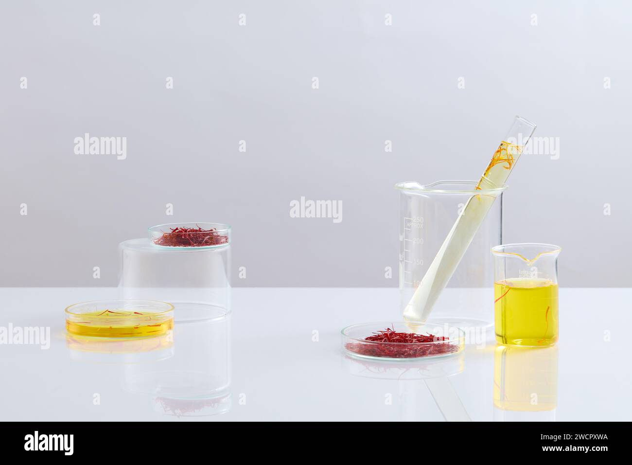 Vetreria da laboratorio contenente zafferano e liquido decorata su sfondo bianco. La gente mangerebbe lo zafferano per aumentare l'umore e migliorare la memoria Foto Stock