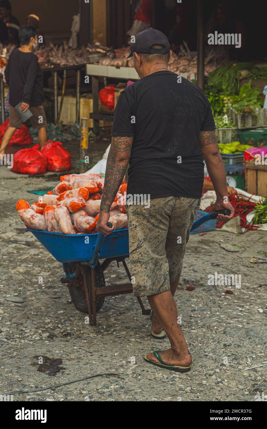 Balikpapan, Indonesia - 11 gennaio 2024. Un uomo sta consegnando un carrello pieno di carne di pollo al venditore del mercato. Foto Stock
