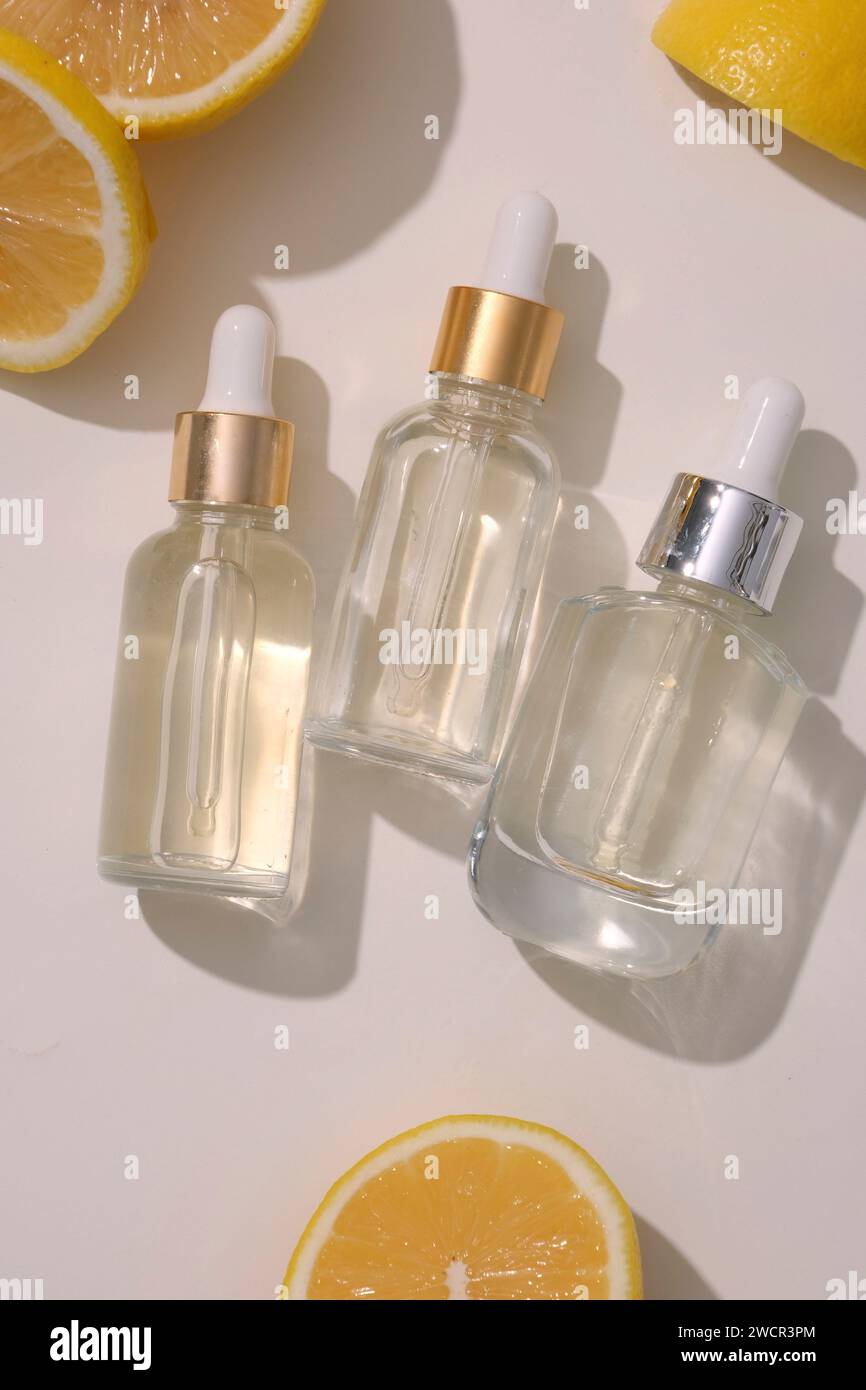 Tre flaconi contagocce in vetro trasparente senza etichetta disposti su sfondo bianco con alcune fette di limone. Il limone (Citrus limon) ha qualiti astringente Foto Stock