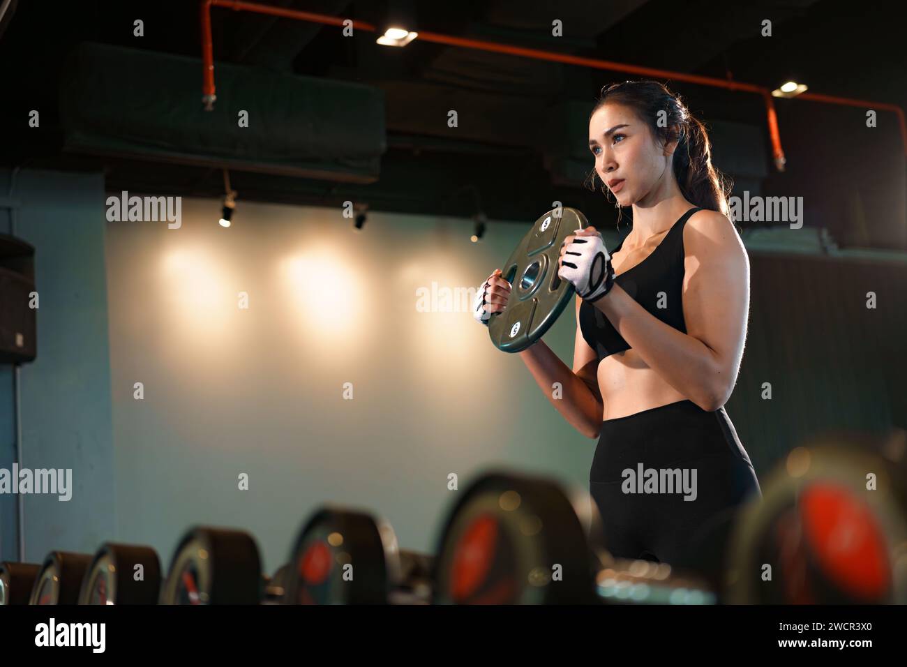 Donna sportiva che fa esercizi con piatti per pesi pesanti in palestra. Foto Stock
