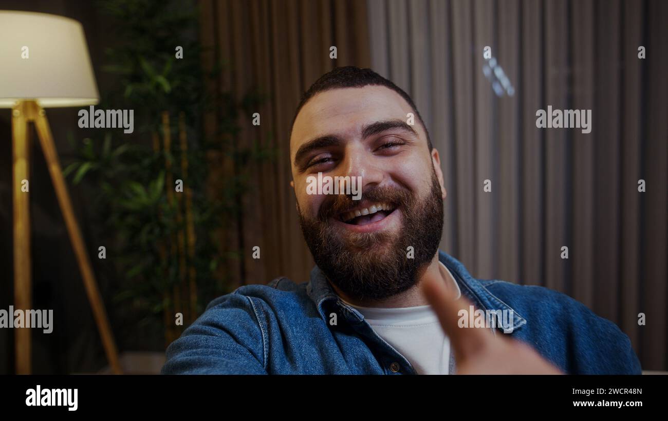 Selfie di un giovane adulto sorridente che tiene in mano uno smartphone e guarda la fotocamera mentre effettua una videochiamata o un selfie Foto Stock