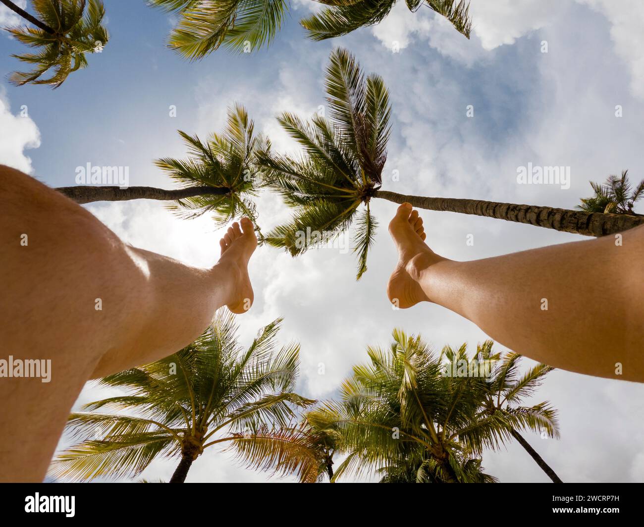 Giovane con le gambe che puntano verso il cielo blu con palme e nuvole Foto Stock
