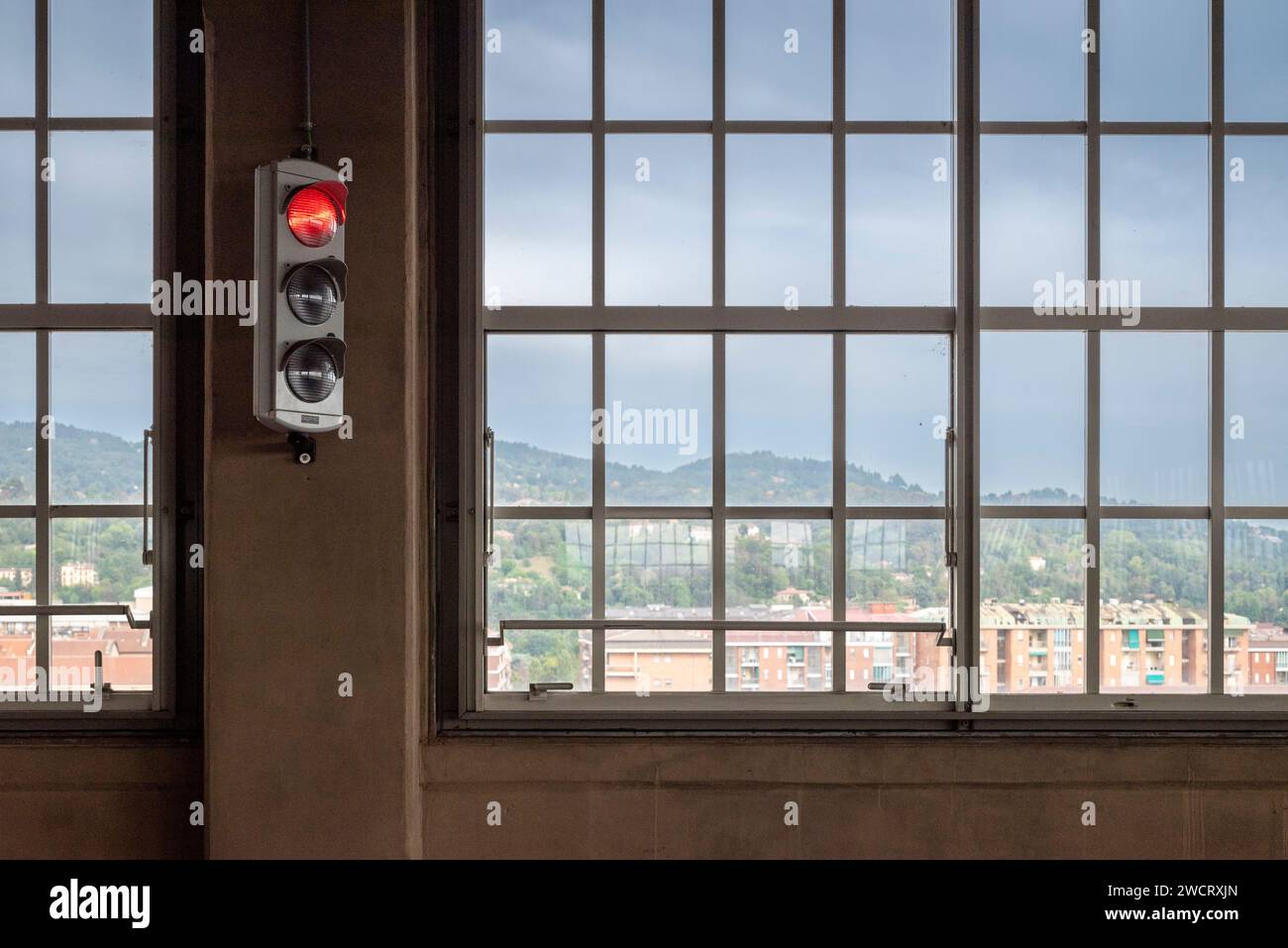 Semaforo rosso in primo piano accanto a una finestra, vetrate colorate, con un panorama della città e delle colline. Foto Stock