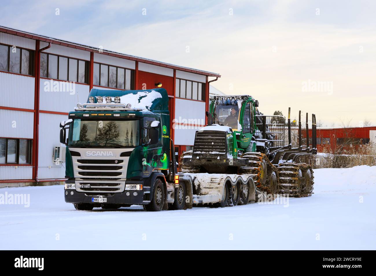 Caricamento dello spedizioniere forestale John Deere 1210E sul rimorchio del dumper Scania G490 per il trasporto in un giorno d'inverno. Salo, Finlandia. 27 dicembre 2023. Foto Stock