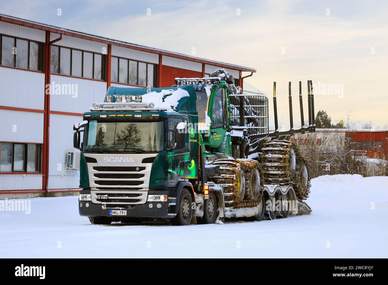 Caricamento dello spedizioniere forestale John Deere 1210E sul rimorchio del dumper Scania G490 per il trasporto in un giorno d'inverno. Salo, Finlandia. 27 dicembre 2023. Foto Stock