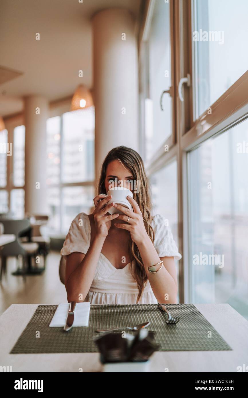 Una donna attraente che si gode un momento vicino alla finestra, assaporando una tazza di caffè appena fatto Foto Stock