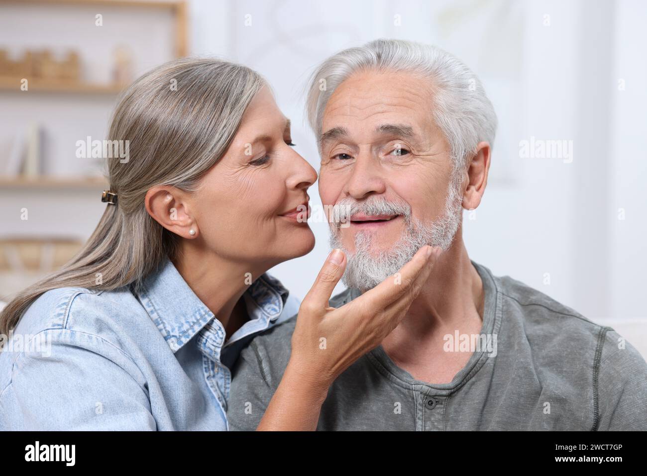 Donna anziana che bacia il suo amato uomo al chiuso Foto Stock