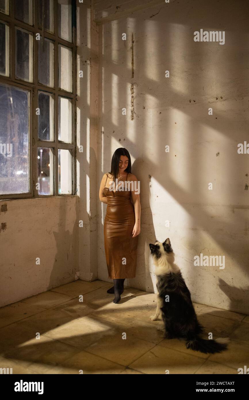 In una stanza leggermente illuminata, una donna sta guardando lontano con un grande cane seduto con attenzione al suo fianco Foto Stock