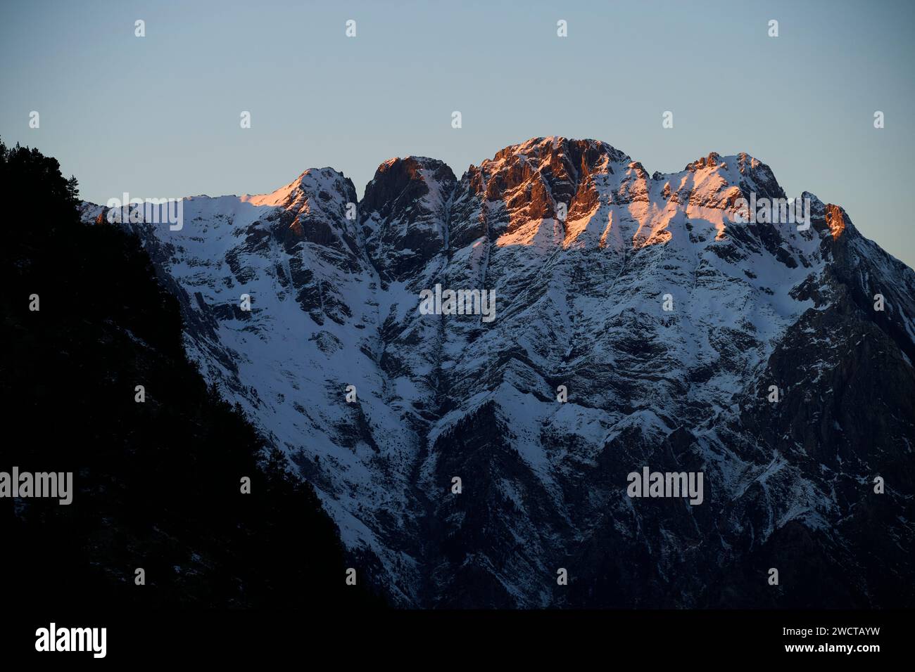 Le cime innevate delle montagne si crogiolano nel caldo bagliore del sole che tramonta con ombre contrastanti Foto Stock