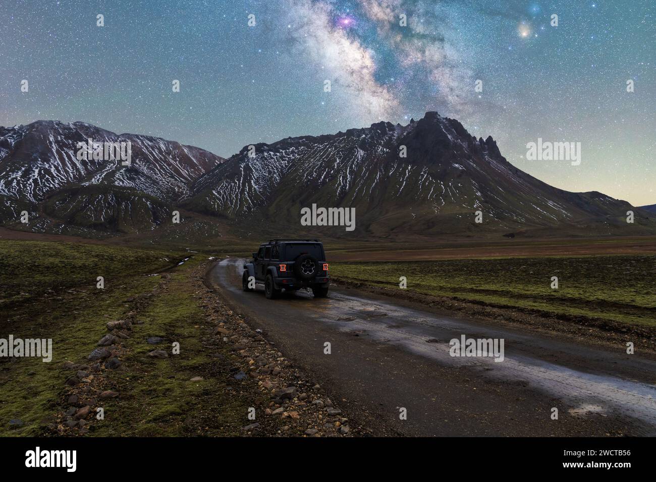 Veicolo fuoristrada parcheggiato su un sentiero di ghiaia con uno sfondo di montagne innevate sotto la via Lattea in Islanda di notte Foto Stock