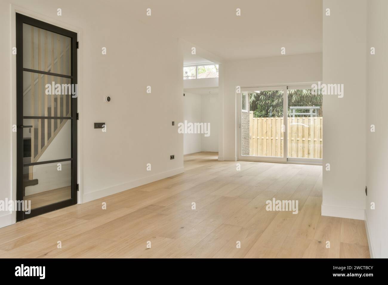 'Camera spaziosa e moderna con grandi finestre, pavimenti in legno e pareti neutre, che attendono mobili e decorazioni.' Foto Stock