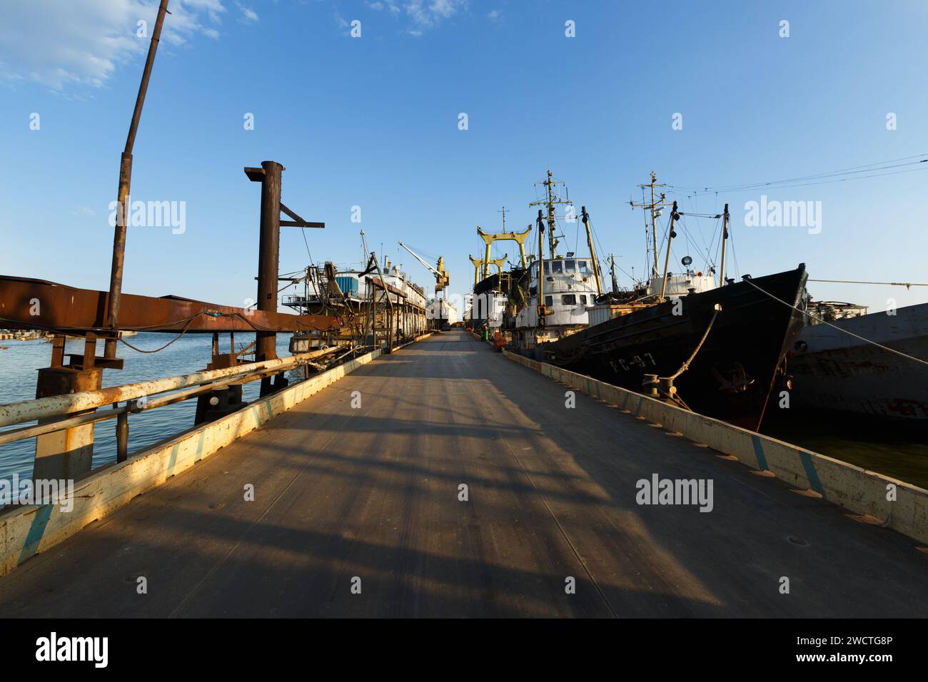 Il ponte di pontone conduce ai cantieri navali, le navi sono sottoposte a riparazioni sotto il cielo limpido. Le infrastrutture marittime industriali supportano il commercio e i trasporti. Carreggiata Foto Stock